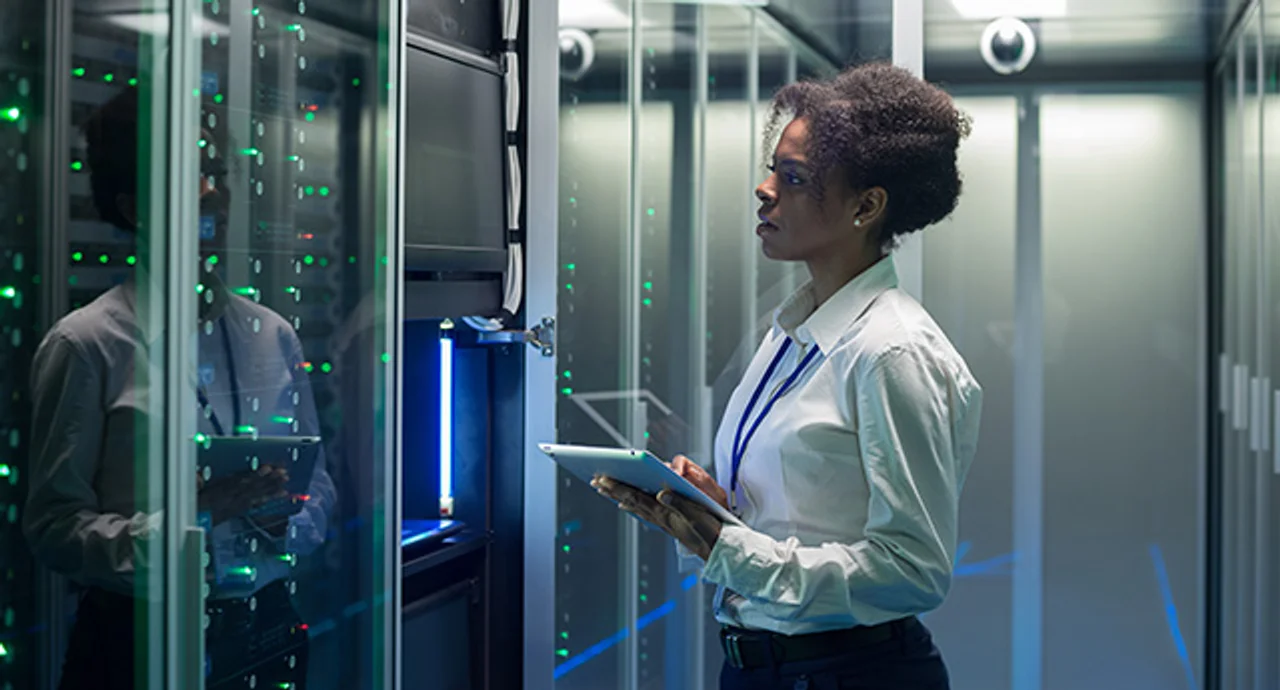 Medium shot of female technician working on a tablet in a data center full of rack servers running diagnostics and maintenance on the system